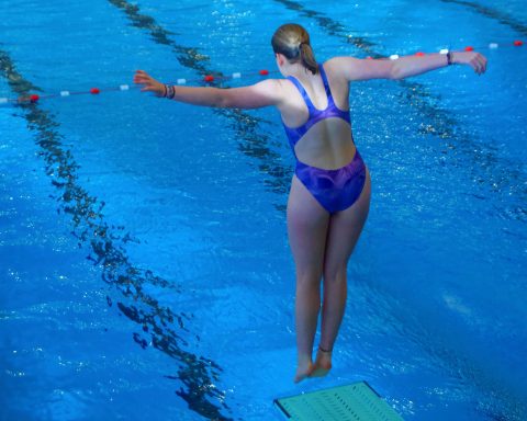 Eine junge Wasserpringerin steht am Sprungbrett und ist für den Absprung ins Wasser bereit.