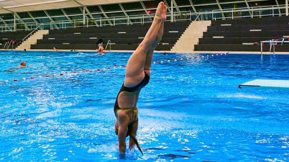 Eine junge Wasserspringerin taucht gerade nach ihrem Sprung ins Wasser ein.