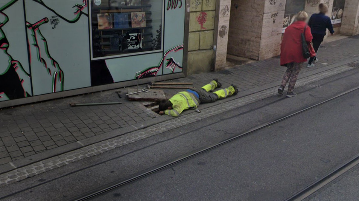 Ein Arbeiter liegt am Boden, weil er etwas in einem Gulli repariert.